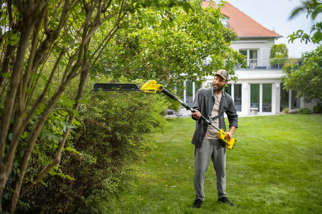 Mann schneidet Hecke im Garten mit Heckenschere