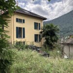 Gelbes Haus mit grünen Fensterläden und Bergkulisse