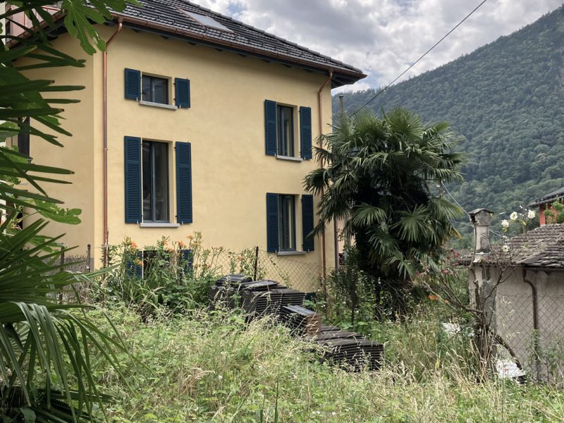 Gelbes Haus mit grünen Fensterläden und Bergkulisse